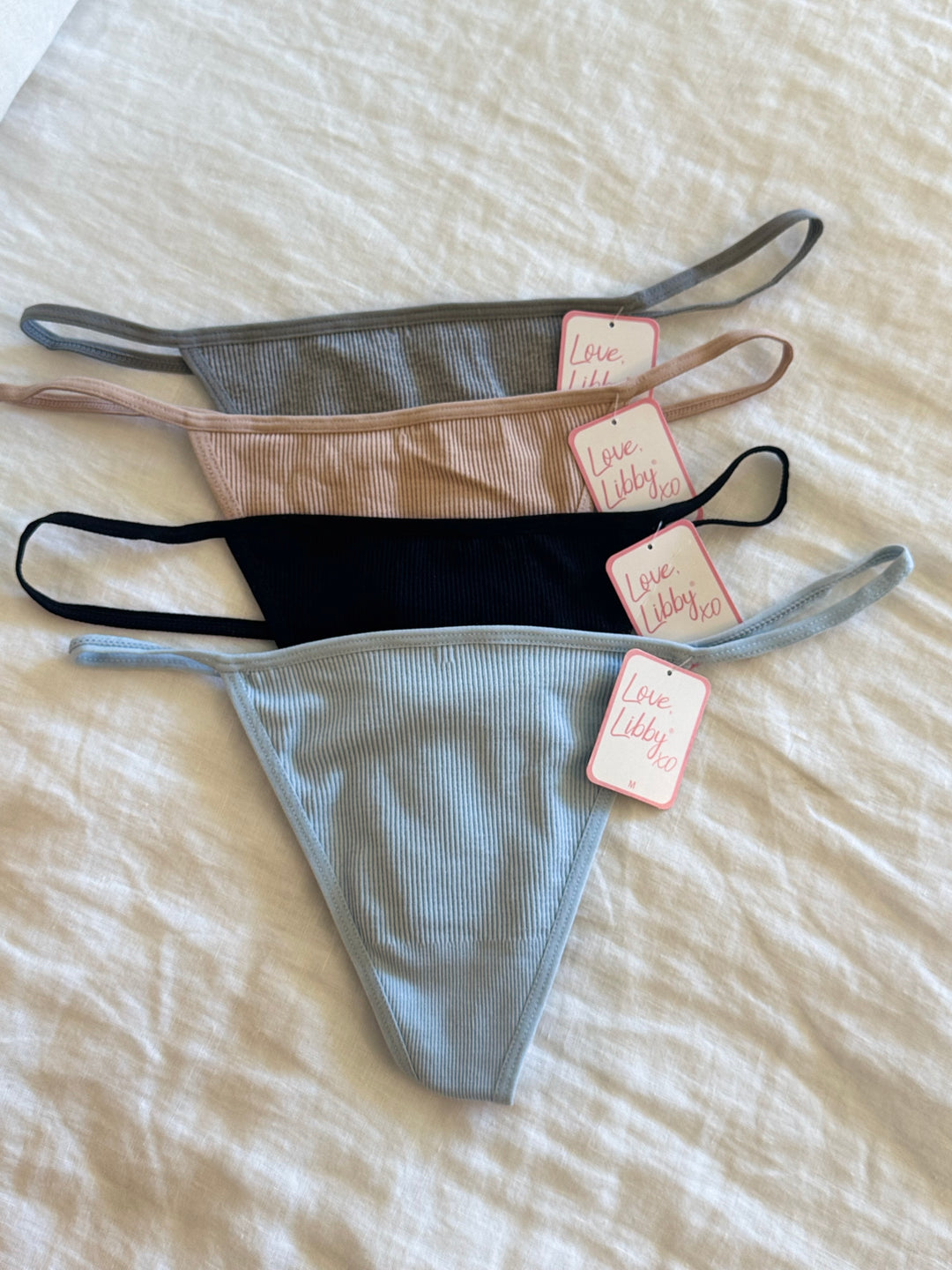 Three pairs of underwear in gray, black, and beige with tags on a beige surface.